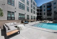 Modern apartment building with chic outdoor patio featuring stylish seating, inviting pool, and relaxing sunbeds under a clear sky.