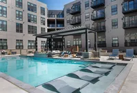 Luxurious apartment complex with a modern outdoor pool area, stylish lounge chairs, and cozy seating under a pergola.