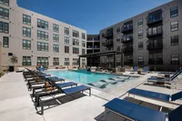 Modern luxury apartment complex with an inviting outdoor pool area, ample sun loungers, and stylish seating, ideal for relaxation and entertainment.