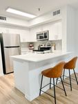 Designed to Inspire Every Meal Modern kitchen with sleek white cabinetry, stainless steel appliances, and a stylish breakfast bar with brown leather stools.