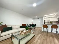 Modern Living with a Cozy Touch Bright and modern living space featuring a cozy sofa, elegant glass coffee table, and a stylish kitchen with a breakfast bar and high-end appliances.