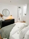 Your Sanctuary Awaits Chic bedroom with elegant decor featuring a cozy bed, stylish black dresser, and a modern ensuite bathroom.