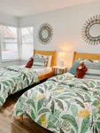 Sleep In, Stretch Out Bright and charming bedroom with twin beds, tropical-themed bedding, warm wooden furniture, and decorative round mirrors creating a cozy, inviting atmosphere.