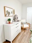 Extra room, extra comfort Chic bedroom nook with a modern white dresser topped with greenery and books, complemented by a cozy armchair with a soft elephant plushie accent. The space is adorned with a stylish palm tree artwork, creating a serene and welcoming atmosphere.