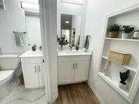The Perfect Blend of Form & Function Bright and modern bathroom with dual sinks, elegant white cabinetry, and stylish shelving with decor for a refreshing ambiance.