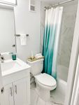Clean, Crisp, and Contemporary Elegant bathroom with modern fixtures, featuring a sleek white vanity, turquoise ombre shower curtain, and marble tile accents.