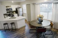 Style That Flows from Kitchen to Table Chic kitchen and dining area featuring stainless steel appliances, modern white cabinetry, and cozy breakfast bar with stools. Bright dining nook with round table and elegant flower centerpiece.