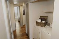 Laundry Spaces Designed to Work for You with Extra Storage Where You Need It Most Inviting apartment hallway leading to a modern bathroom, featuring elegant wood flooring and a convenient laundry area with stylish storage.