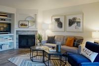 Open Spaces. Endless Possibilities. Chic living room with modern decor, featuring a cozy fireplace, stylish grey sofa with vibrant pillows, elegant artwork, and a warm, inviting atmosphere.