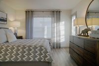 Your Sanctuary Awaits Inviting bedroom with abundant natural light, featuring elegant decor, plush bedding, and a stylish dresser accented by a decorative lamp.
