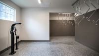 Smart, Secure, and Ready to Roll Modern and spacious bike storage room with gleaming speckled flooring, ample hanging racks, and natural light.