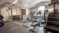Your Gym, Just Steps from Home Modern fitness center with state-of-the-art gym equipment, including treadmills, weight machines, and a StairMaster, illuminated by natural light through large arched windows.
