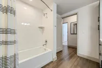 Inviting bathroom with elegant white tiles, a chic shower and tub combo, and stylish wood flooring, creating a serene oasis.
