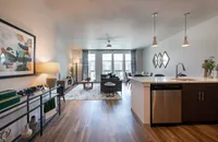 Chic open-concept living space with sleek wood flooring, modern kitchen island, and elegant dining area. Bright natural lighting enhances the cozy yet sophisticated ambiance.