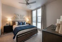 Elegant bedroom with modern decor, featuring a cozy bed, stylish nightstands, and large windows with sheer curtains.