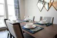 Elegant dining area with a modern table set for four, featuring polished wood furniture, stylish tableware, and natural light from large windows.