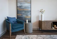 Chic apartment living area showcasing a cozy teal armchair, modern art, and elegant decor on warm wooden flooring.