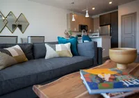 Inviting living space with modern open kitchen, plush gray sofa, vibrant cushions, and elegant wood accents creating a cozy atmosphere.
