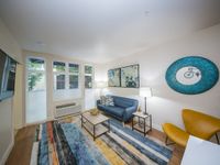 Contemporary living room with abundant natural light, featuring a cozy blue sofa, vibrant artwork, and a stylish rug enhancing the space.