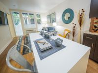 Chic modern apartment dining area with sleek white table, elegant decor, and vibrant accent rug, inviting natural light through large windows.