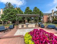 Charming outdoor community space featuring a modern pergola with a grill, surrounded by lush landscaping and comfortable seating.