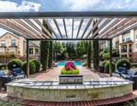 Inviting apartment complex courtyard featuring a pergola with comfortable seating, lush landscaping, and a sparkling pool under a bright blue sky.