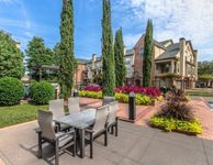 Elegant apartment exterior with lush landscaping, tall trees, and a stylish outdoor dining area.