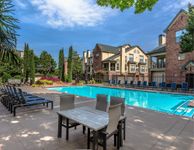 Luxurious apartment community with a stunning outdoor pool, surrounded by elegant lounge chairs, lush landscaping, and charming brick architecture.