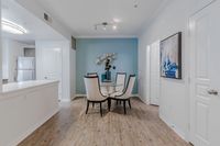 Chic dining area with modern decor, featuring a glass table and elegant chairs, set against stylish blue accent wall in a spacious apartment.