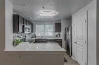 Modern kitchen with sleek dark cabinets, stainless steel appliances, and a spacious countertop, accented by natural light through a large window.