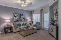 Elegant living room with plush beige sofa, abstract artwork, and stylish glass coffee table under a ceiling fan.