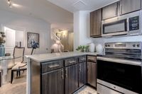 Modern kitchen with sleek stainless steel appliances, marble countertops, and warm wooden cabinetry, adjacent to open dining space with elegant chairs and artful decor.