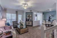 Elegant open-concept living room with cozy seating, sleek glass coffee table, and modern dining area. Bright kitchen view enhances the spacious ambiance.