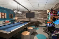 Game Nights Just Got Better Luxury entertainment room featuring a billiards table, arcade games, modern lighting, and cozy seating in a stylish wooden-accented space.