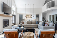 The Heart of the Community Spacious and bright living room with a modern gray sectional sofa, stylish kitchen, high ceilings, and chic pendant lighting.