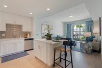 Style That Flows from Kitchen to Table Modern open-concept kitchen and living room with sleek white cabinetry, stylish island seating, and a view of lush greenery through large glass doors.
