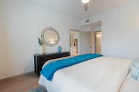 Cozy Bedrooms, Peaceful Nights Inviting bedroom with plush bedding, a stylish mirror, and a sleek dresser, offering a glimpse into a modern open-concept kitchen.