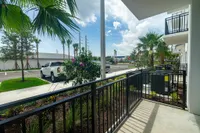 Your Private Outdoor Escape Charming apartment balcony overlooking lush landscaping and a serene suburban street, featuring vibrant plants and palm trees under a bright blue sky.