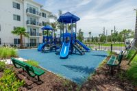 Ready to Play. Built to Impress. Modern apartment complex with a vibrant blue playground, surrounded by lush greenery and palm trees, perfect for family living.