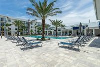Catch Rays or Cool Off Luxurious apartment complex poolside with palm trees, modern sun loungers, and a serene atmosphere under a bright blue sky.