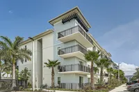 Modern Lines, Timeless Comfort Modern apartment building with spacious balconies, surrounded by lush palm trees under a bright blue sky.