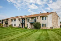 Charming residential complex with beige brick facade, featuring balconies and verdant lawn, ideal for serene living.