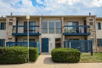 Charming two-story apartment building with modern blue accents, inviting balconies, and lush greenery.
