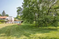 Inviting apartment exterior with lush green lawns, mature trees, and a sparkling pool, perfect for relaxation and leisure.