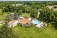 Beautiful aerial view of a residential complex featuring a vibrant community pool, lush green lawns, and ample parking surrounded by serene trees.