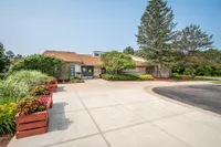 Charming community entrance with lush greenery, vibrant flower planters, and a welcoming clubhouse facade.
