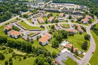 Scenic aerial view of a charming residential community featuring clustered buildings with orange roofs, lush green lawns, and a sparkling swimming pool.