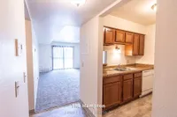 Inviting apartment layout showcasing an open living space with plush carpeting, complemented by a compact kitchen with wooden cabinetry and sleek countertops, ideal for modern living.