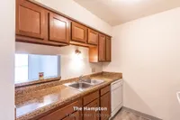 Charming kitchen in The Hampton apartment featuring warm wooden cabinetry, a sleek granite countertop, and modern appliances. 1 Bed, 1 Bath, 630 sq. ft.