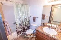 Bright and modern bathroom in 'The Hampton' 1 Bed, 1 Bath apartment, featuring elegant granite countertops, stylish floral shower curtain, and cozy lighting over a spacious mirror.